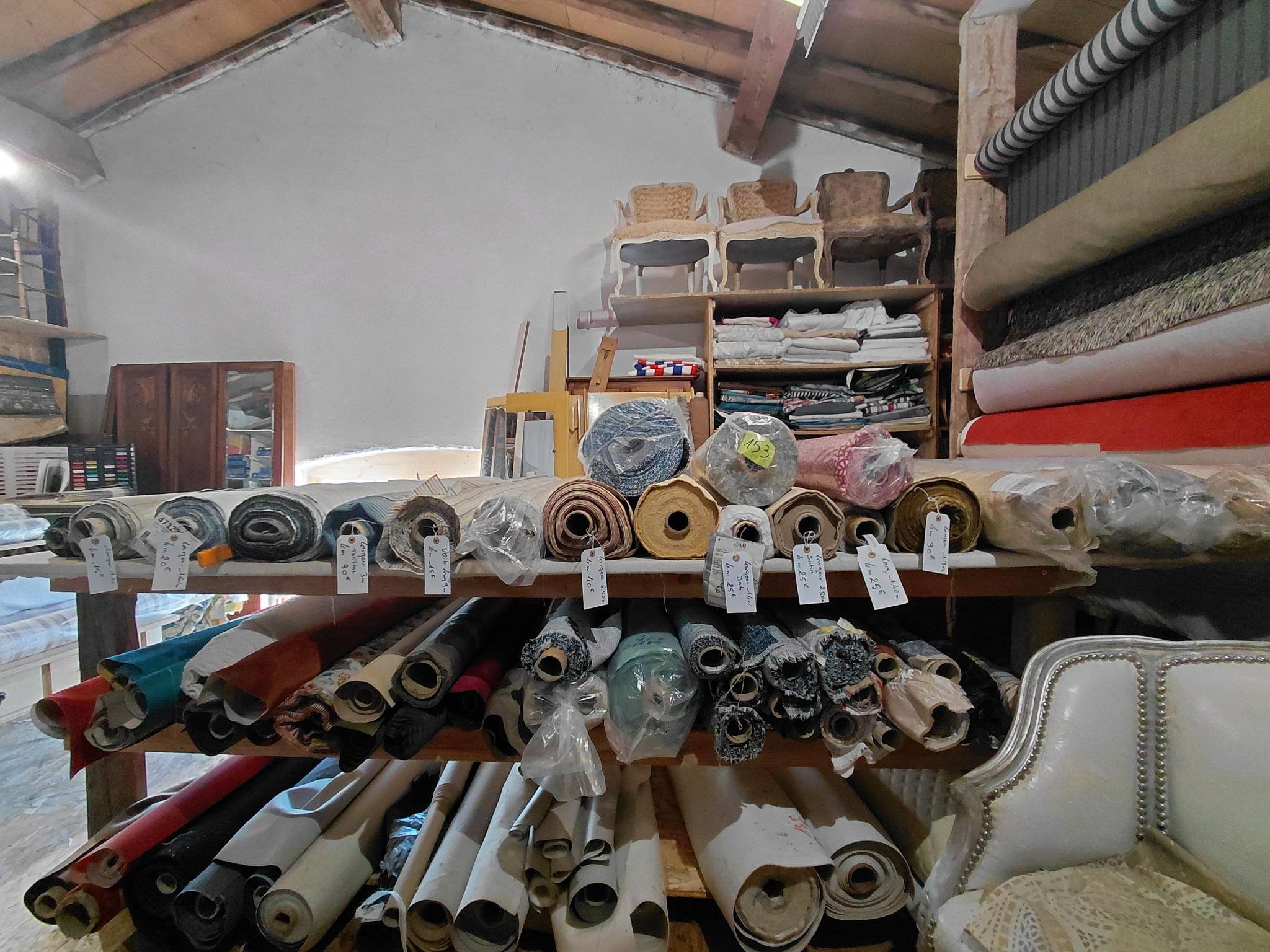 Atelier celadeco à Toulouse avec rouleaux de tissu, chaises en restauration et fauteuil tapissé blanc